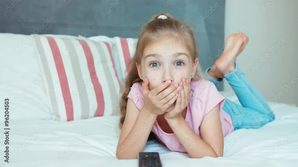 Laughing girl watching TV. Child lying on the bed. Child shocked TV. Big eyes Laughing girl watching TV. Child lying on the bed. Child shocked TV. Big eyes