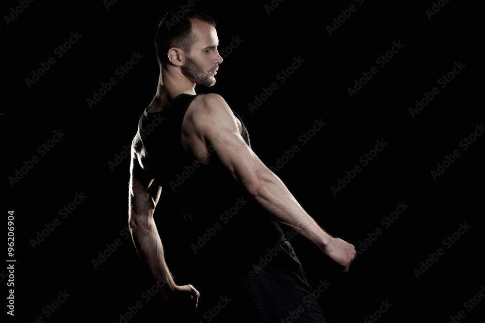 muscular man, clasps hands in fist, black background, place for text on the right muscular man, clasps hands in fist, black background, place for text on the right