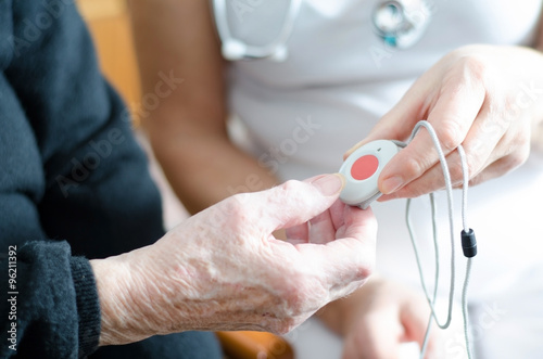 Pflegekraft überreicht älterer Dame einen Notfallknopf