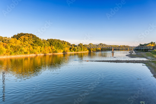 Colorful autumn landscape with the river and railway bridge over dry weather at sunset.