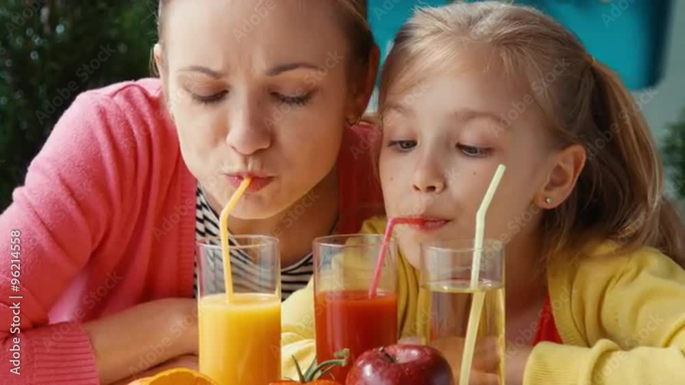Mother and daughter drinking tomato and orange juice and looking at camera