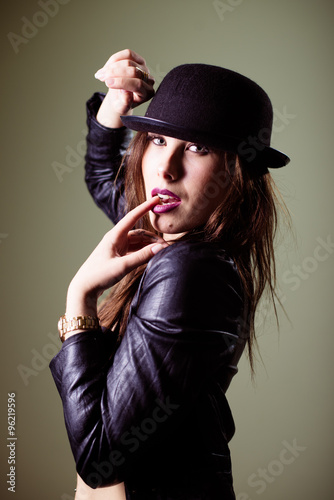 Close up portrait of hot sexy pretty young lady wearing black hat and leather jacket sensually looking at camera on gray copy space background photo