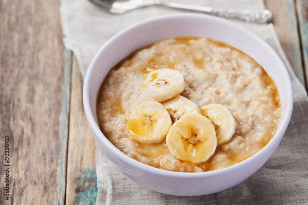 Bowl of oatmeal porridge with banana and caramel sauce on rustic table, hot and healthy breakfast every day, diet food Bowl of oatmeal porridge with banana and caramel sauce on rustic table, hot and healthy breakfast every day, diet food
