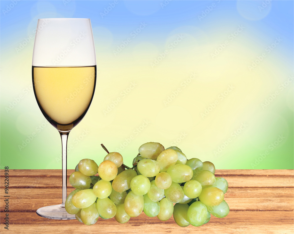 Glass of white wine and green grape on wooden table over nature