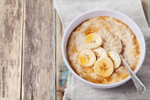 Bowl of oatmeal porridge with banana and caramel sauce on rustic table, hot and healthy breakfast every day, diet food
