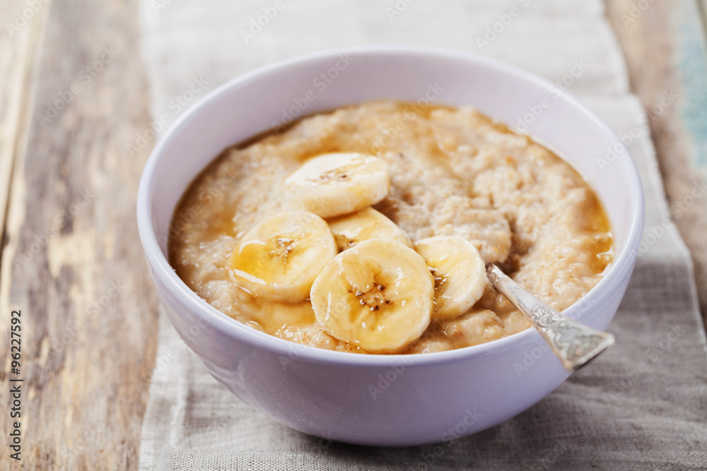 Bowl of oatmeal porridge with banana and caramel sauce on rustic table, hot and healthy breakfast every day, diet food Bowl of oatmeal porridge with banana and caramel sauce on rustic table, hot and healthy breakfast every day, diet food
