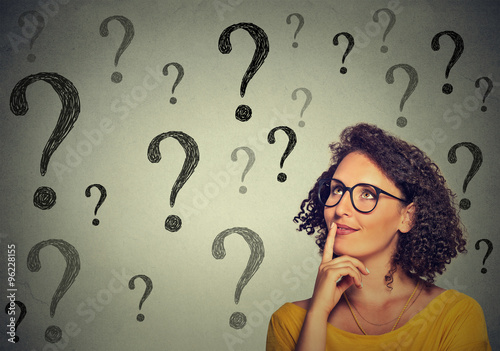 Thinking young business woman in glasses looking up at many question marks
