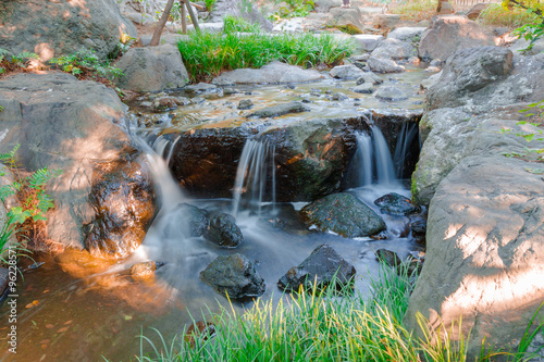 Water falls over a jumble of moss-covered boulders in forest.