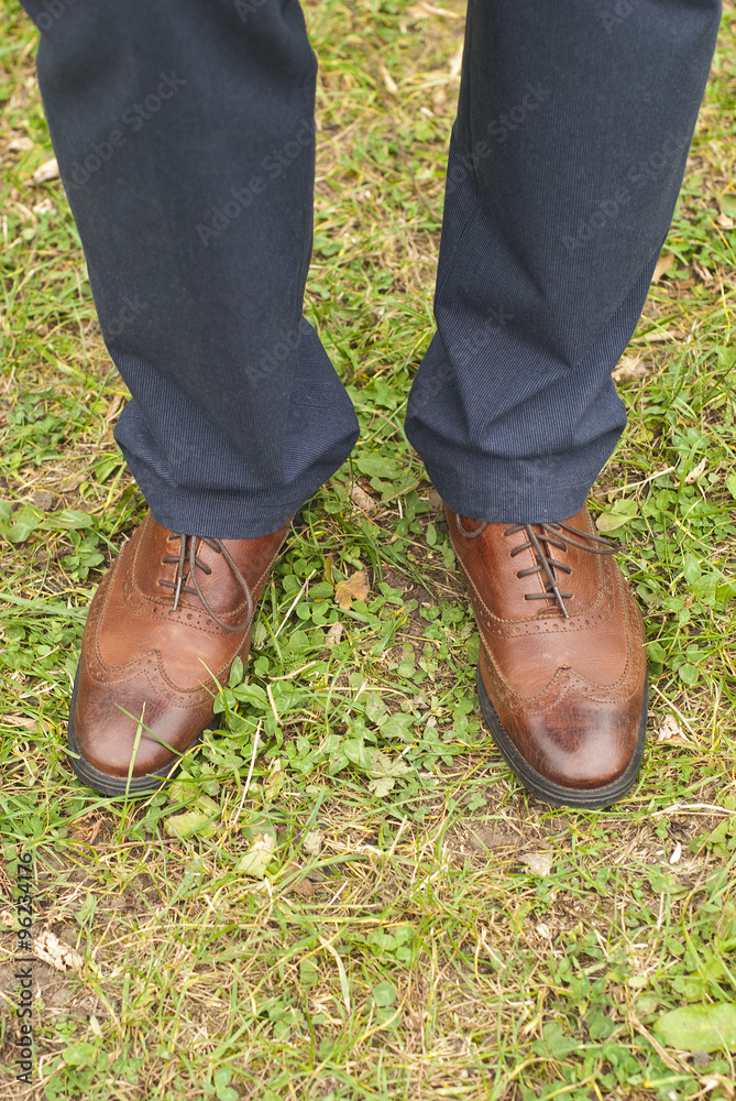 Young fashion man's legs in blue jeans and brown boots on grass 