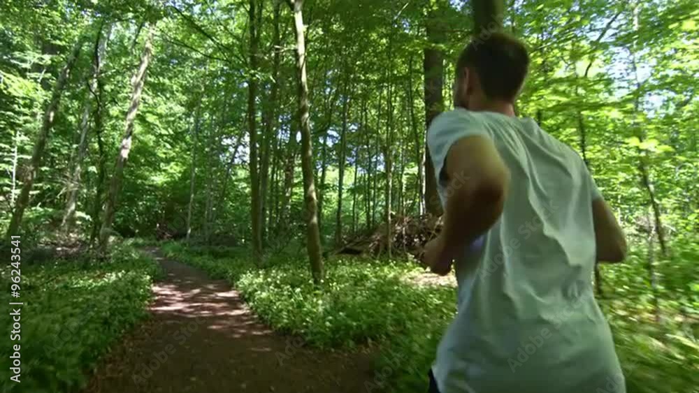 Tracking shot of fit young man running through trees in forest representing healthy lifestyle Tracking shot of fit young man running through trees in forest representing healthy lifestyle