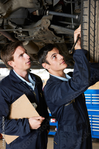 Mechanic And Trainee Working Under Car