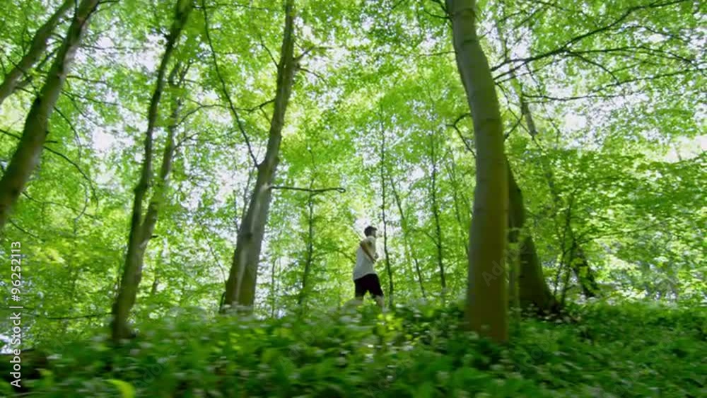 Panning shot of sporty young man running through trees in forest Panning shot of sporty young man running through trees in forest
