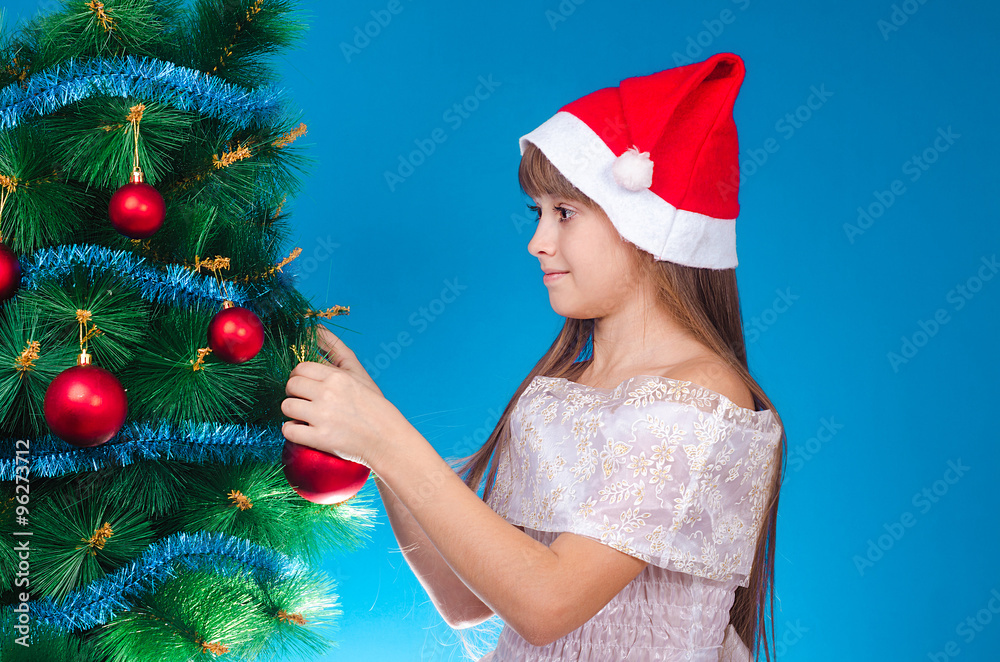 The girl with long hair in a red cap hangs up a toy on a beautiful New Year tree and smiles. New year. Christmas.
