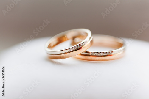 Golden wedding rings with diamonds on white background. Symbol of love and marriage.