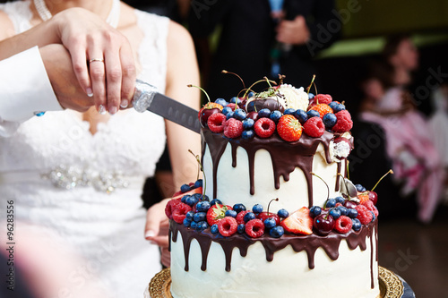Cutting the wedding cake with berries