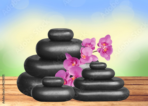 Black spa stones and pink orchid on wooden table over nature bac