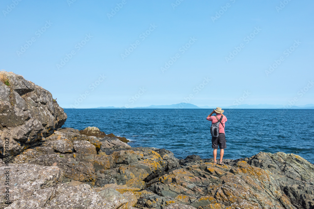 Man looking into the distance on the Pacific Ocean with binoculars off the coast of Vancouver Island, Canada
