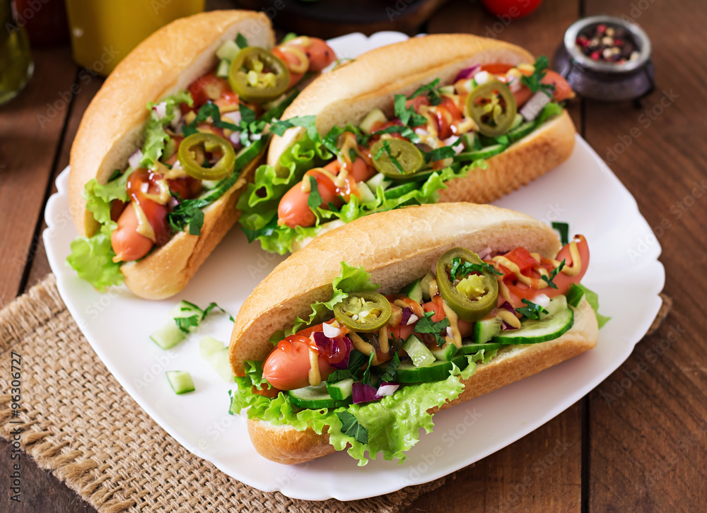 Hot dog with jalapeno peppers, tomato, cucumber and lettuce on wooden background Hot dog with jalapeno peppers, tomato, cucumber and lettuce on wooden background
