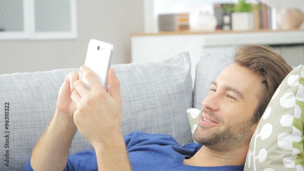Man relaxing in sofa looking at smartphone Man relaxing in sofa looking at smartphone
