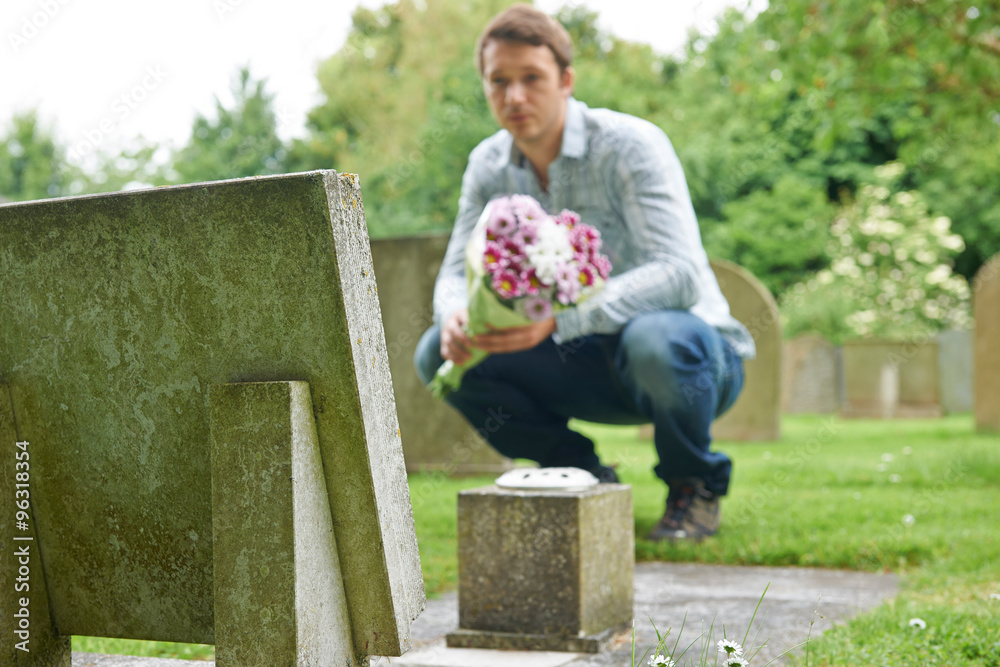 Man Placing Flowers By Headstone In Cemetery Man Placing Flowers By Headstone In Cemetery