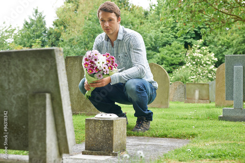 Man Placing Flowers By Headstone In Cemetery photo