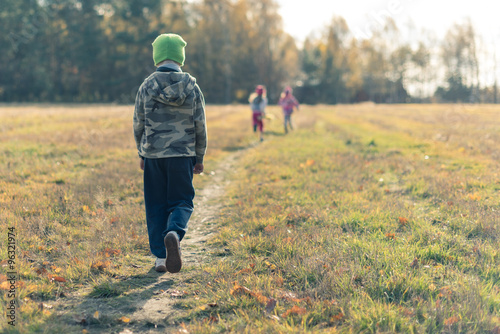 Sad boy walking behind laughing children