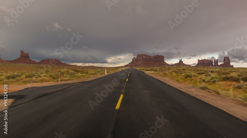 Driving USA: Dramatic point of view POV shot of empty lonely road and stormy skies over Monument Valley, Arizona Utah
