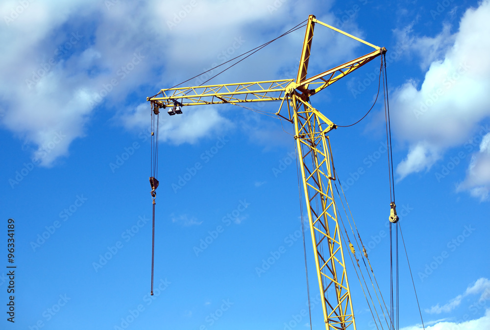 Yellow tower construction crane over clear blue sky with light white clouds Yellow tower construction crane over clear blue sky with light white clouds