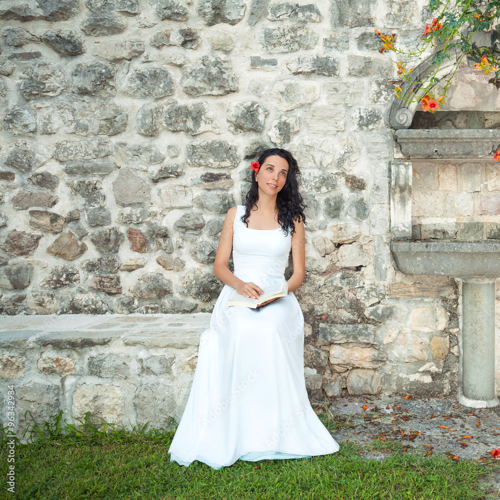 Portrait of a beautiful young woman reading a book in the rustic formal garden