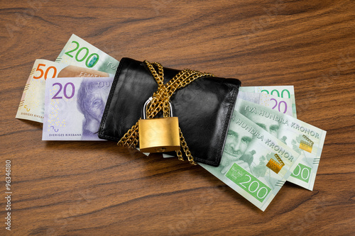 Swedish banknotes sticking out from a black wallet with chain and lock. On wooden walnut background. photo