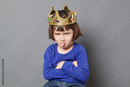spoiled kid concept - cheeky preschool child with golden crown on head folding arms and sticking out tongue for disrespectful mollycoddled little king or queen metaphor,studio shot