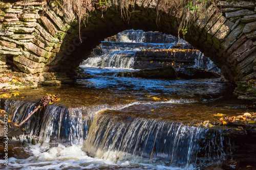 Fototapeta Naklejka Na Ścianę i Meble -  Waterfalls in the stream with an old arched bridge