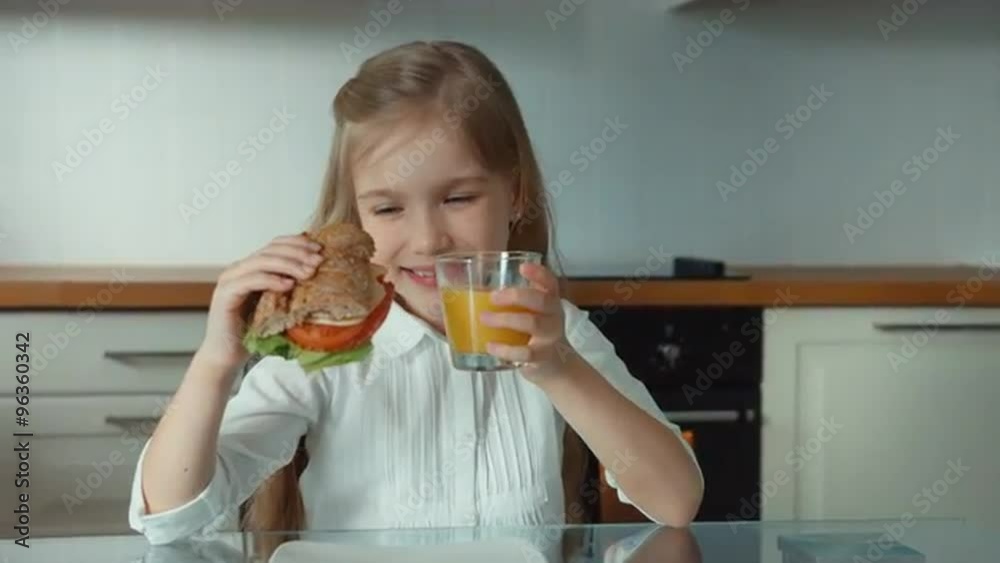 Satisfied child girl holding a sandwich and a glass of orange juice Satisfied child girl holding a sandwich and a glass of orange juice