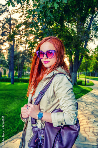 Redhead woman in casual clothing posing outdoors in 60th fashion  sunglasses and bright violet handbag
