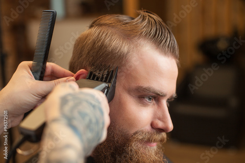 Cheerful bearded guy is getting hairstyle at beauty shop