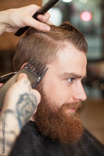 Skillful male barber is working with electric razor