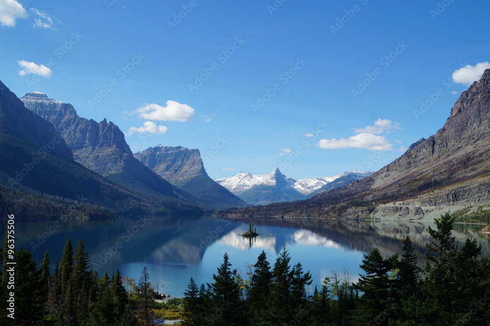 View over a small island in Glacier National Park, USA. The mountains and clouds are reflected in the water.