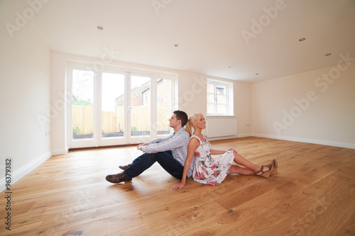 Young Couple Sitting In Empty Room Of Dream House