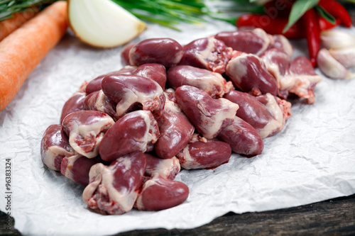 Raw Duck hearts on crumpled paper, decorated with vegetables. on old wooden table.