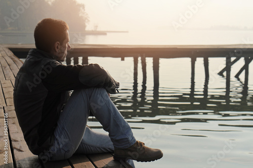 Man sitting on old wooden dock and looking at lake horizon. Thinking, contemplation  relaxing, concentration, loneliness concept photo