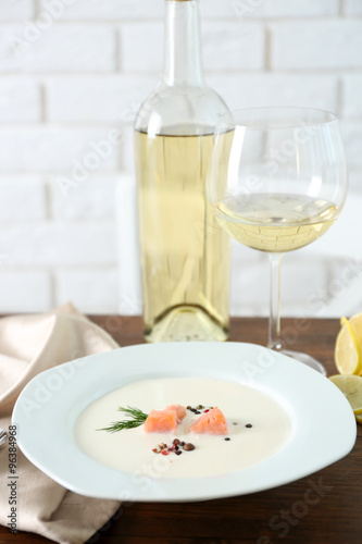 Served wooden table with tasty salmon cream soup, wine and lemon on it, close up