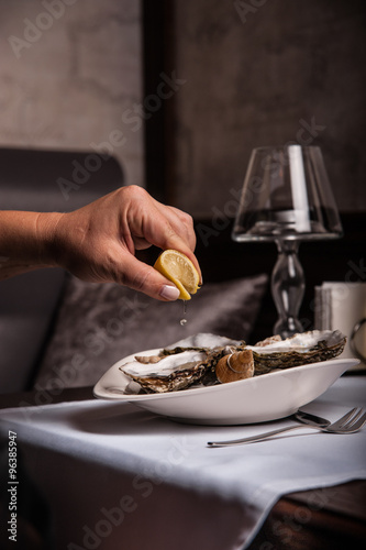 Is squeezed lemon juice to shellfish, which lie in a plate on the table.