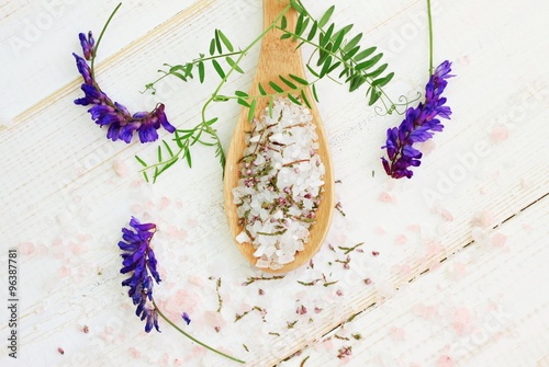 Pink and white bath epsom salt mixture in wooden spoon, fresh and dried aroma herbs. Wooden surface, top view destressing mineral spa background.  photo