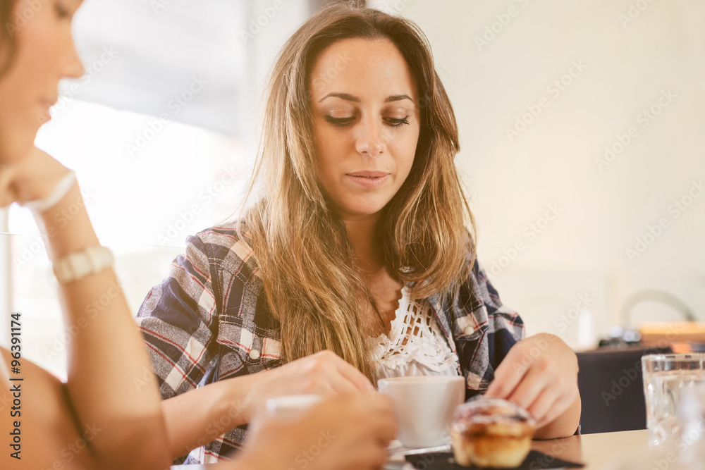 Two young and beautiful women meet at the bar for a cappuccino and to chat. Both look their cup