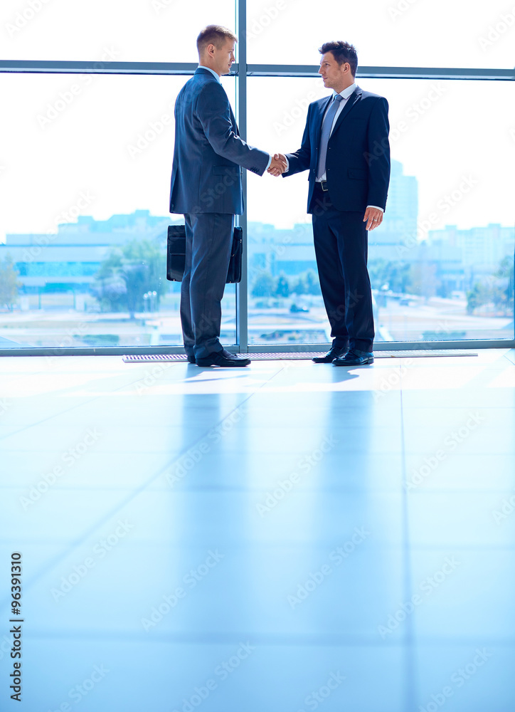 Full length image of two successful business men shaking hands with each other Full length image of two successful business men shaking hands with each other