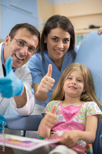 Young girl with dentist and his assistant show thumb up and smil