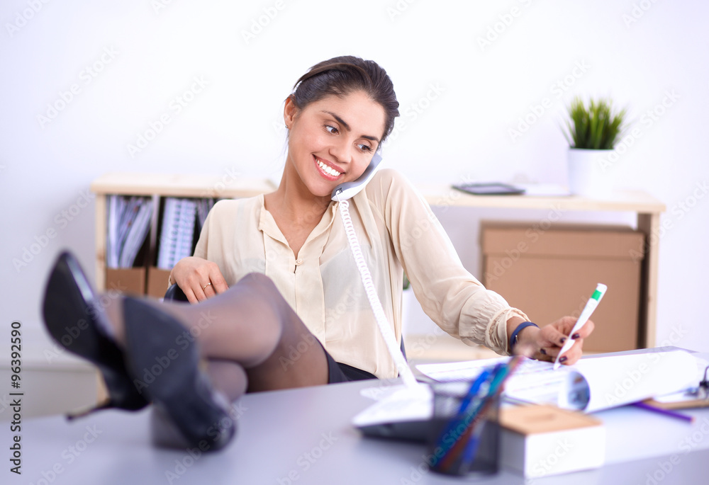 Young businesswoman sitting at the desk and talking on phone Young businesswoman sitting at the desk and talking on phone