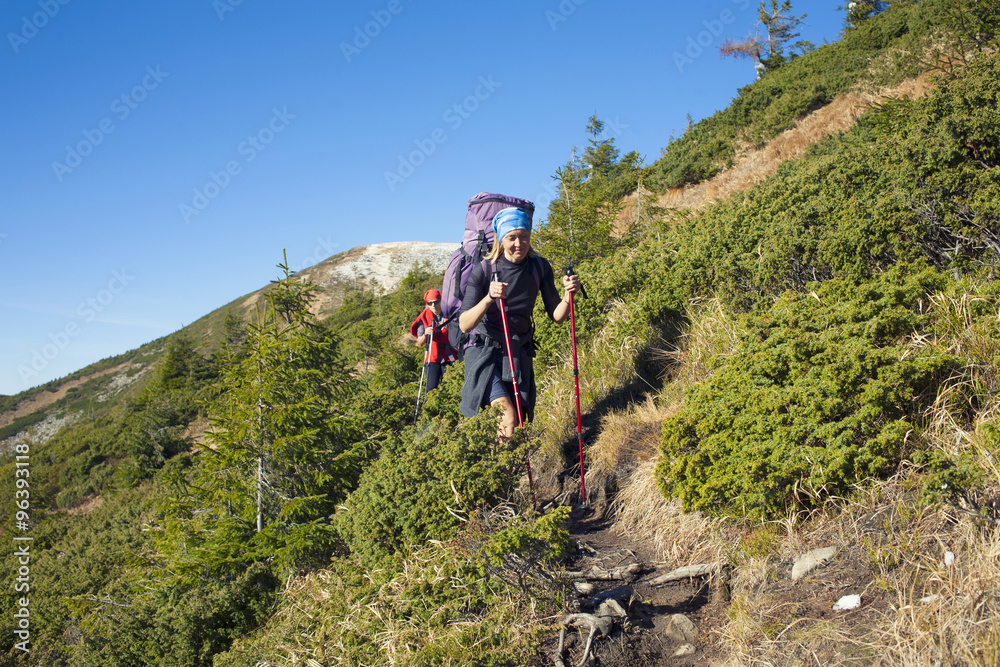 Fototapeta premium Two girls with backpacks walk along a trail.
