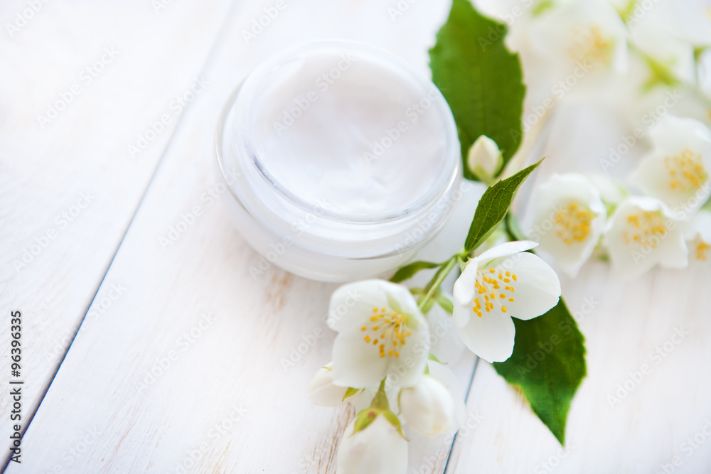 Pot of beauty cream with flower petals on white wooden table