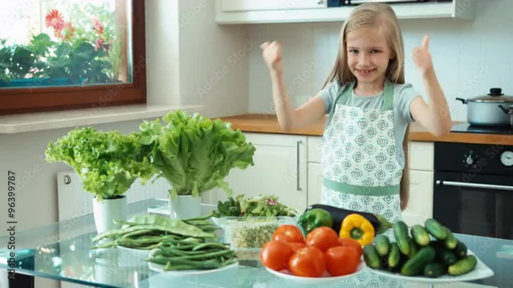 Young chef with vegetables near kitchen table and smiling at camera. Girl promoting healthy food. Thumbs up. Ok Young chef with vegetables near kitchen table and smiling at camera. Girl promoting healthy food. Thumbs up. Ok